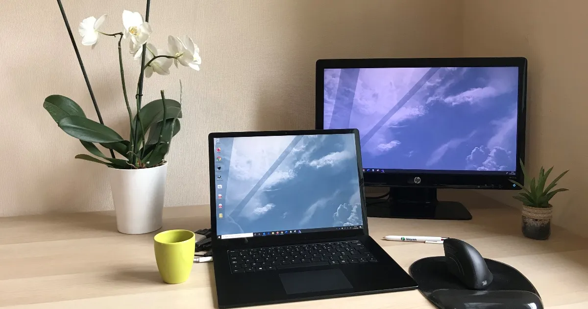 Poste de télétravail : ordinateur portable, écran, orchidée, tasse et stylo Veyan sur un bureau