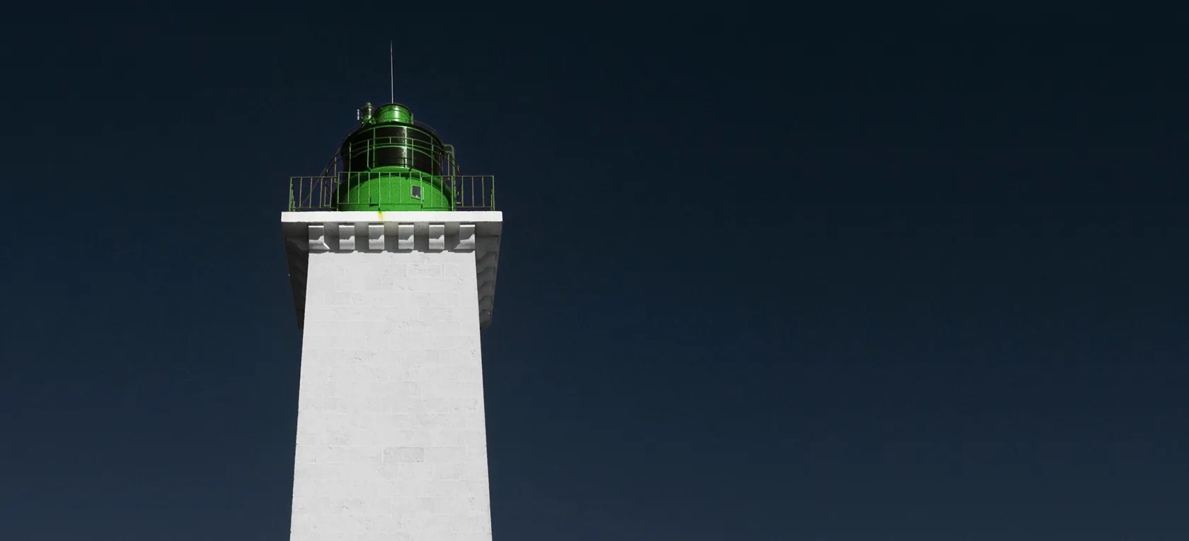 Sommet d’un phare blanc à lanterne verte sur un ciel bleu nuit