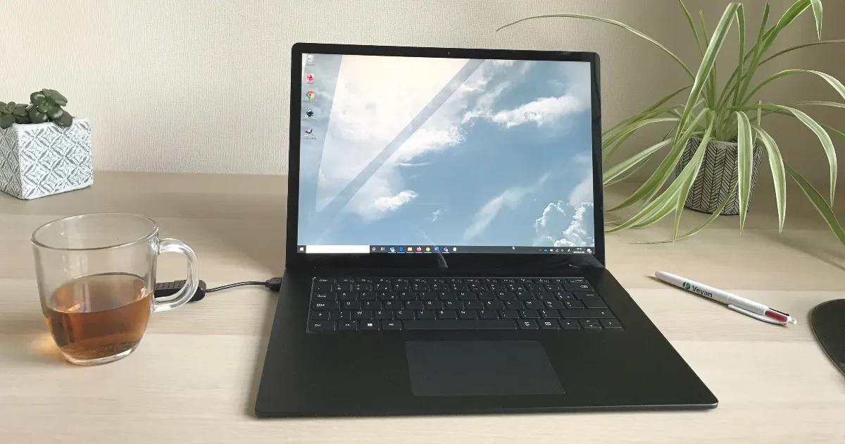 Ordinateur portable ouvert sur un bureau en bois, avec une tasse de thé, une plante et un stylo Veyan