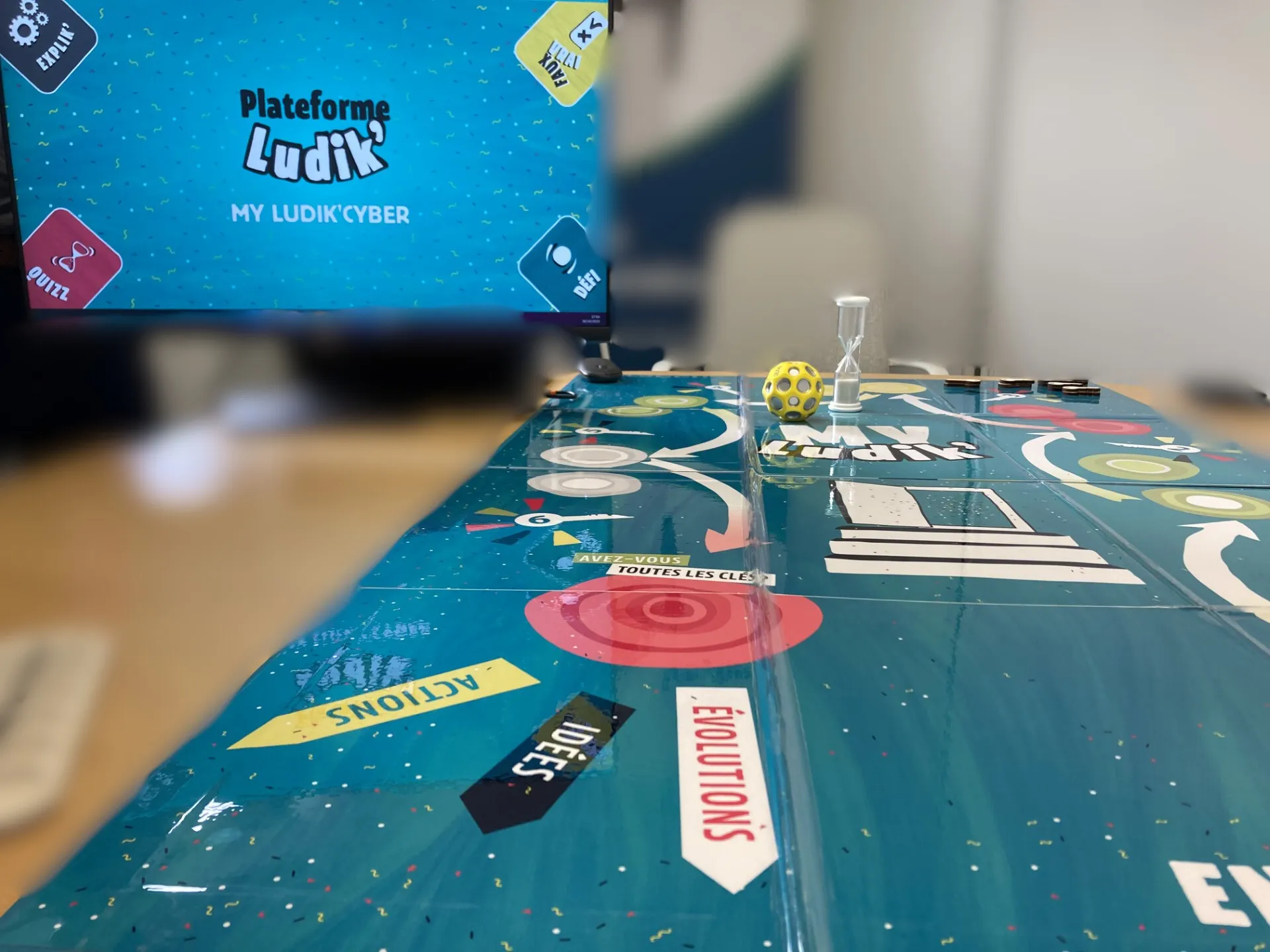 Plateau du jeu My Ludik’Cyber sur une table, avec un sablier, une balle et l’écran de la plateforme Ludik’